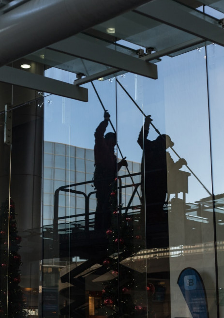 Hombre en una plataforma elevadora realizando tareas de limpieza de cristales en un edificio corporativo